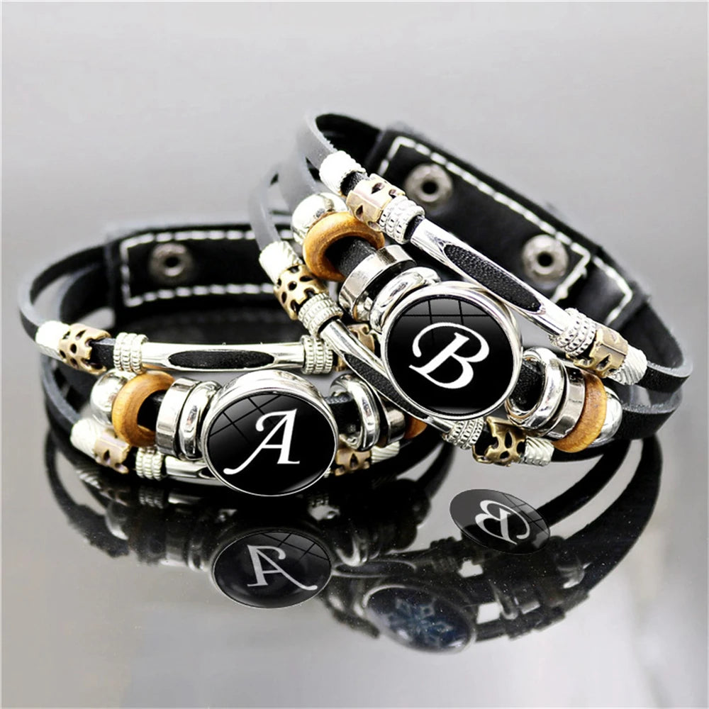 Black leather bracelet with silver, gold, and black beads featuring letters on a reflective surface.