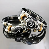 Black leather bracelet with silver, gold, and black beads featuring letters on a reflective surface.