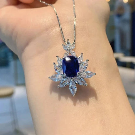 Blue gemstone pendant on a silver chain held by a hand against a blurred background