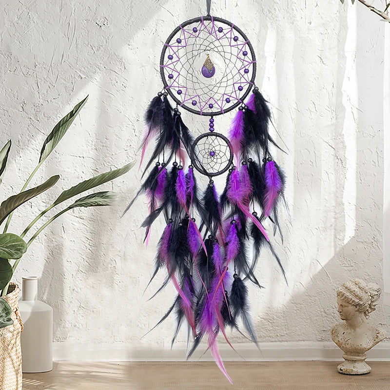 Decorative dreamcatcher with purple and black feathers hanging against a white wall.