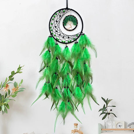 Green dreamcatcher with feathers hanging on a white wall.