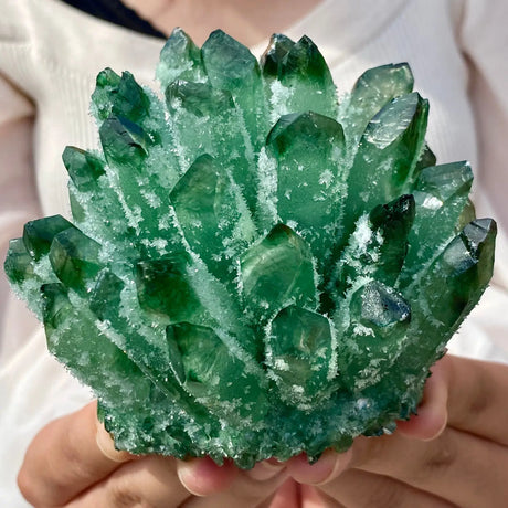 Green crystal formation held in hands against a neutral background