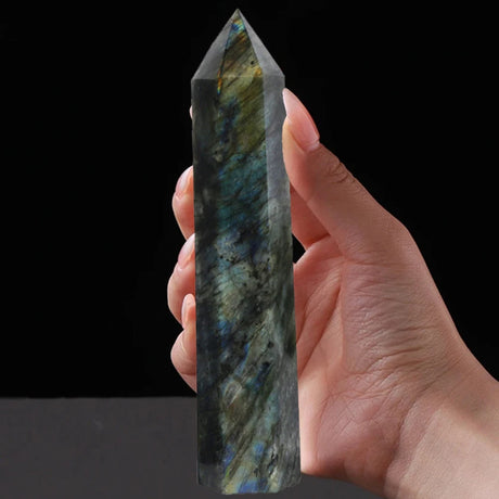 Hand holding a labradorite crystal against a black background