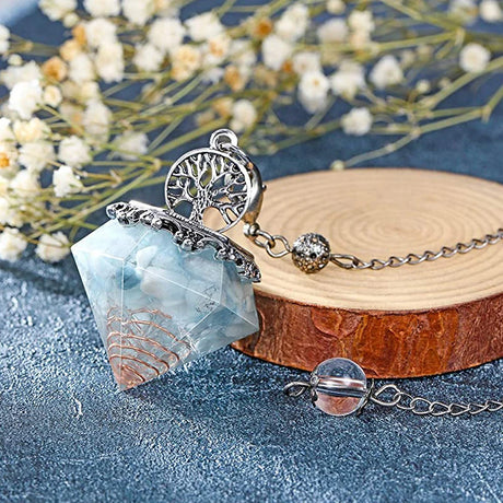 Necklace with a tree of life pendant and blue stone on a wooden block with flowers in the background