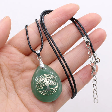 Green pendant with silver tree design on a black cord held in a hand against a white background
