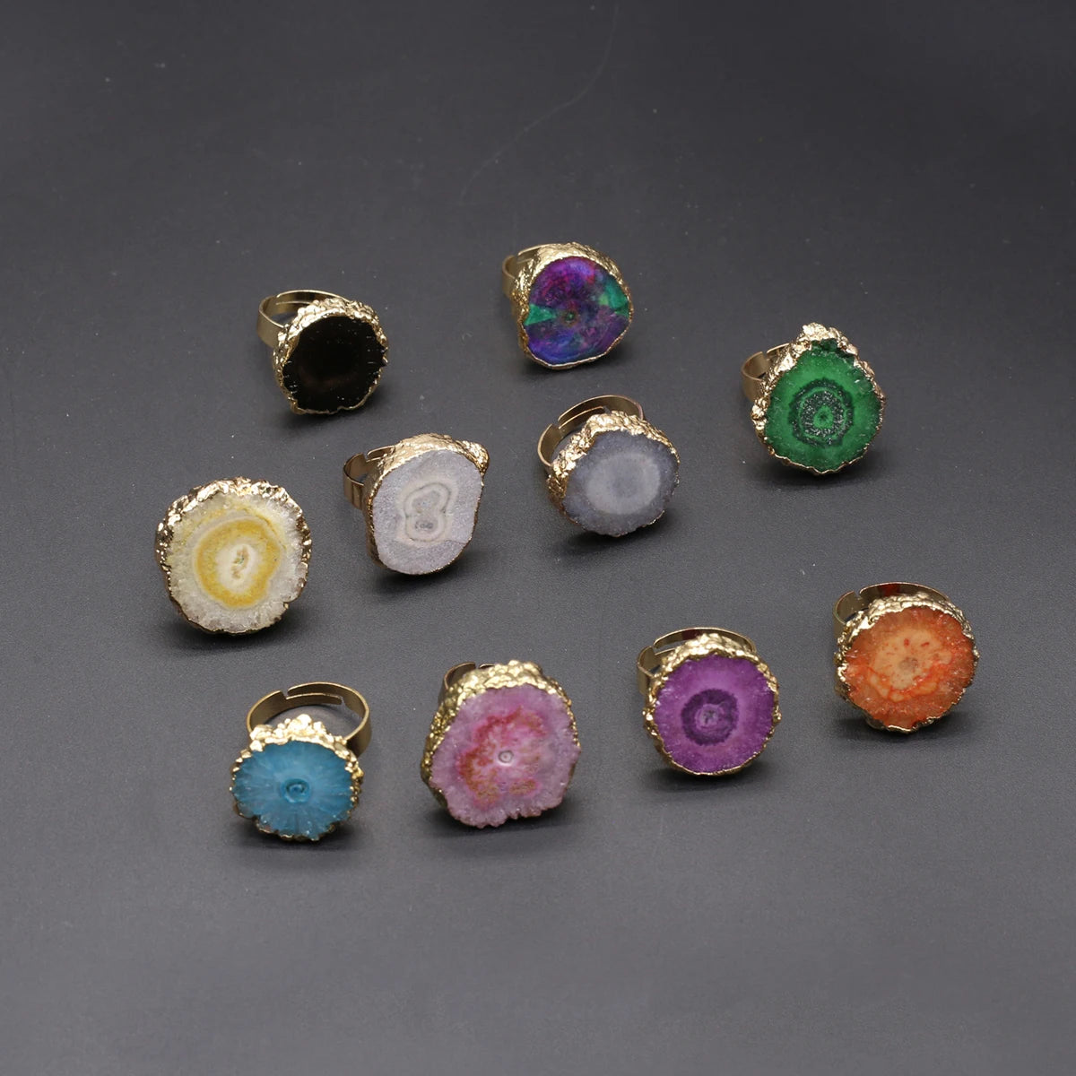 Collection of colorful rings with gold bands on a gray background
