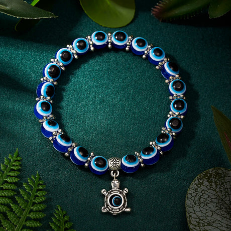 Blue and black beaded bracelet with a silver turtle charm on a green background