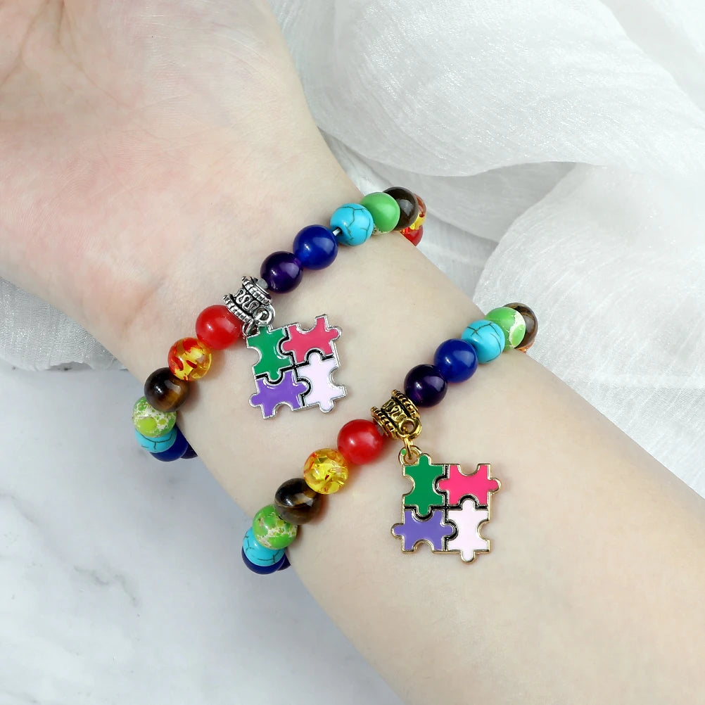 Colorful beaded bracelet with puzzle piece charms on a wrist against a white background