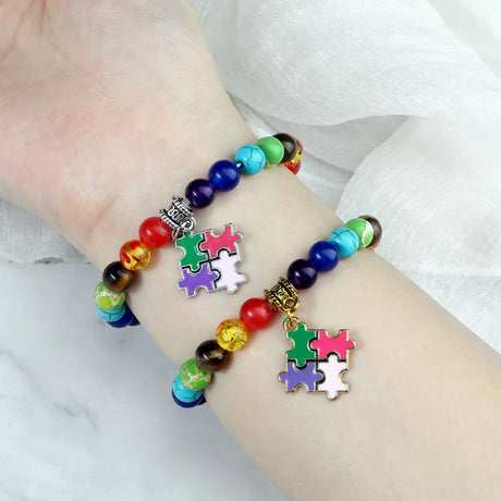 Colorful beaded bracelet with puzzle piece charms on a wrist against a white background