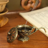 Bronze incense burner with smoke on a wooden surface next to an open book