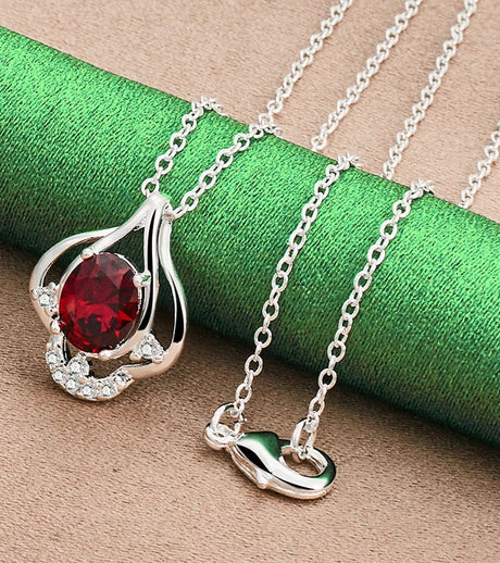 Silver necklace with a red gemstone pendant on a green and brown textured background