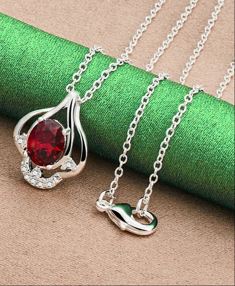 Silver necklace with a red gemstone pendant on a green and brown textured background
