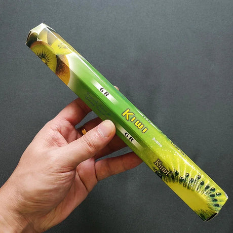 Hand holding a green kiwi fruit packaging against a dark background