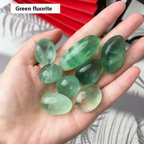 Hand holding green fluorite stones with a red fan in the background