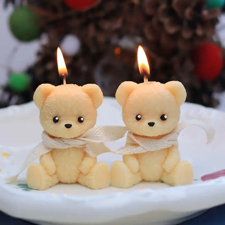 Two teddy bear-shaped candles with lit wicks on a white plate.