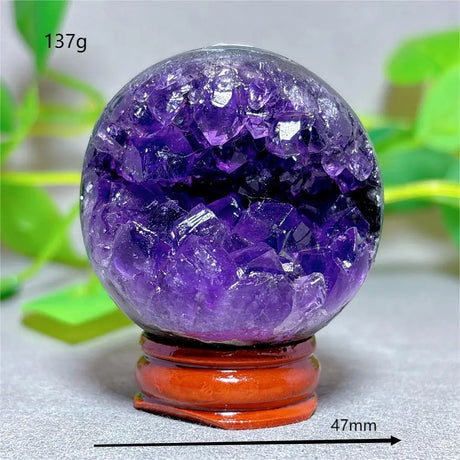 Purple crystal sphere on a wooden stand with green leaves in the background