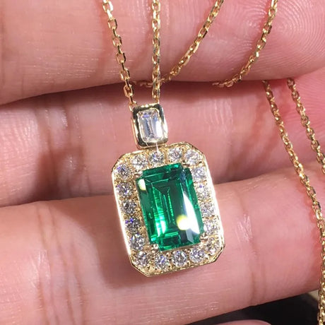 Gold necklace with a green gemstone pendant held between fingers.