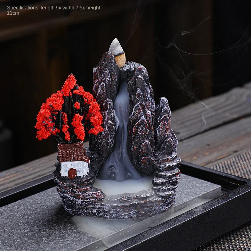 Decorative scene with a mountain, tree, and small house on a dark surface.