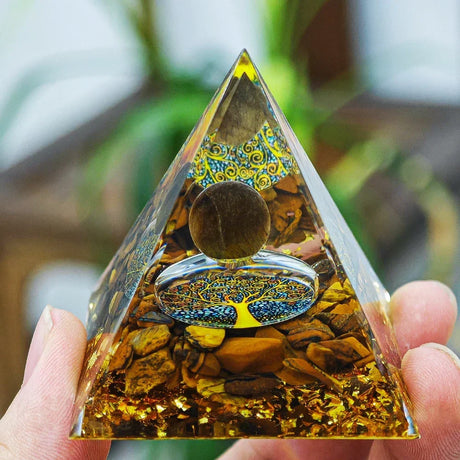 Pyramid-shaped crystal with tree of life design held by a hand against a blurred natural background