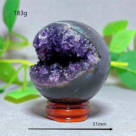 Amethyst geode crystal sphere on a stand with green leaves in the background