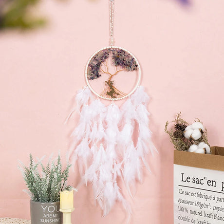 Decorative dreamcatcher with feathers against a pink background
