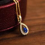 Gold necklace with a blue teardrop pendant on a wooden surface