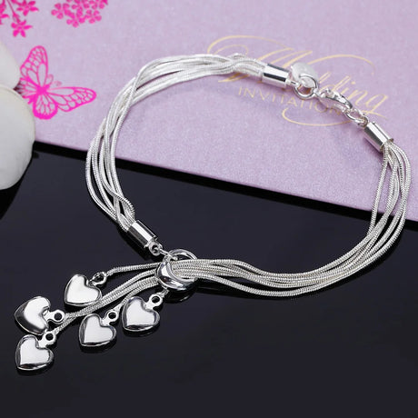Silver bracelet with heart charms on a black surface with a pink card in the background