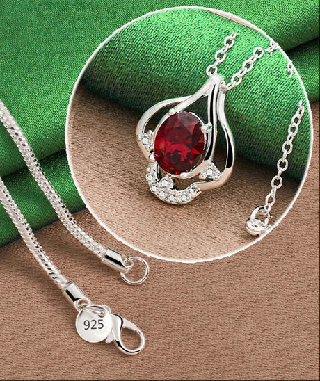 Silver necklace with a red gemstone pendant on a green and brown fabric background