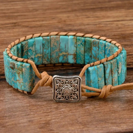 Turquoise beaded bracelet with brown leather strap and silver clasp on a wooden surface
