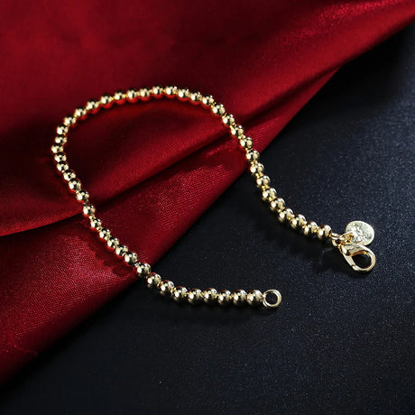 Gold beaded bracelet with a clasp on a dark surface with red fabric