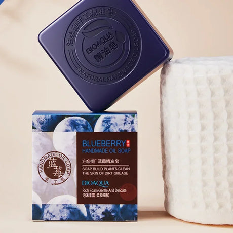 Blueberry handmade oil soap with packaging and a white container on a beige background