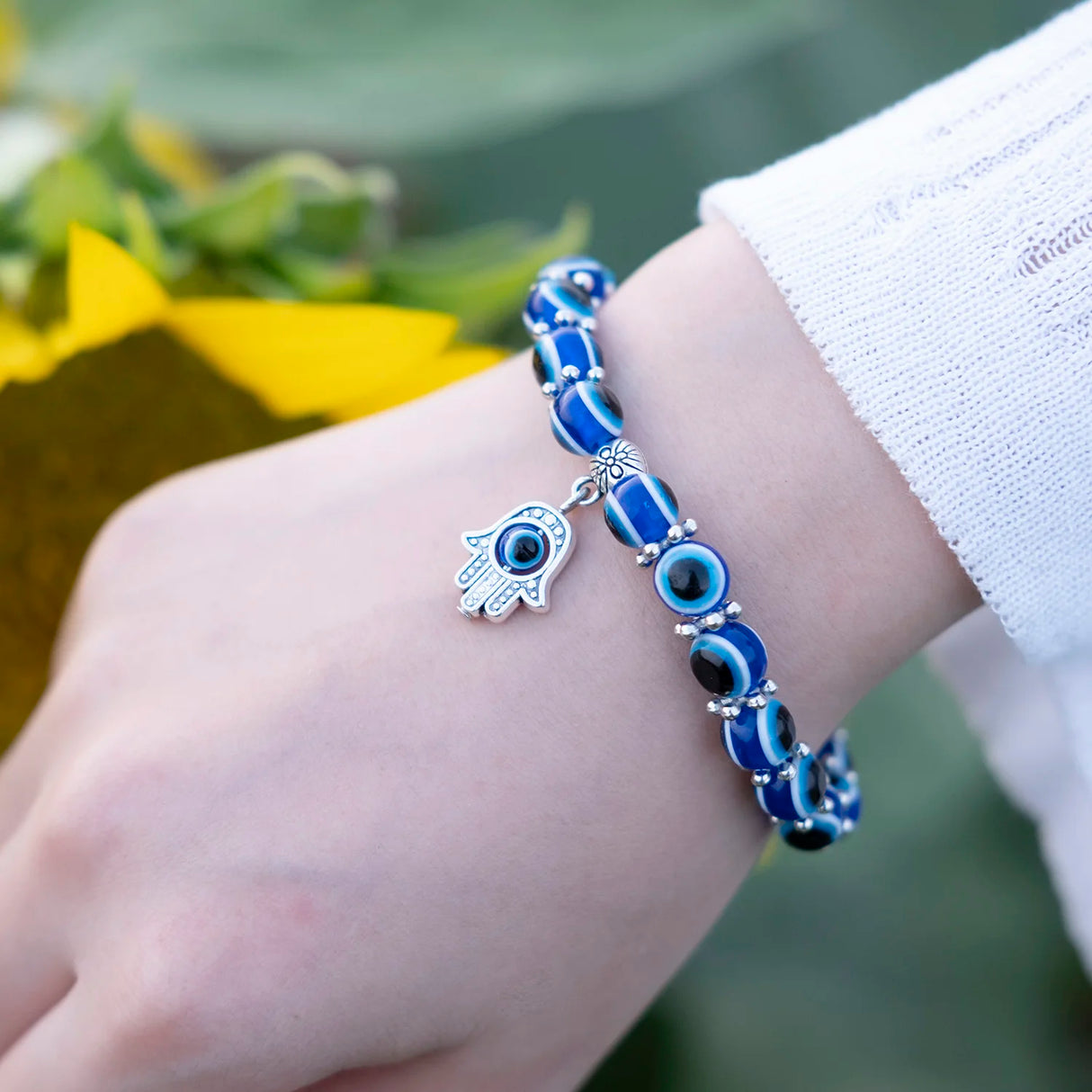 Blue beaded bracelet with a hamsa charm on a wrist, blurred green background