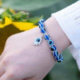 Blue beaded bracelet with a hamsa charm on a wrist, blurred green background