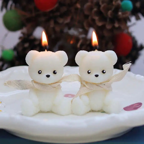 Two teddy bear-shaped candles on a plate with a blurred festive background.