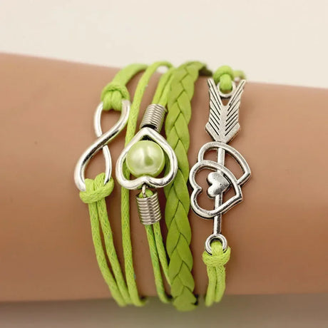 Green braided bracelet with silver heart and arrow charms on a wrist against a beige background