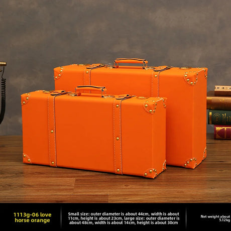 Three orange suitcases of different sizes on a wooden surface with a dark background.