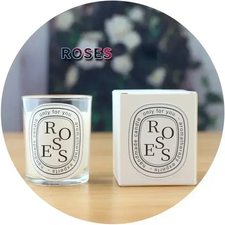 Candle and packaging labeled 'ROSES' on a wooden surface with a blurred floral background.