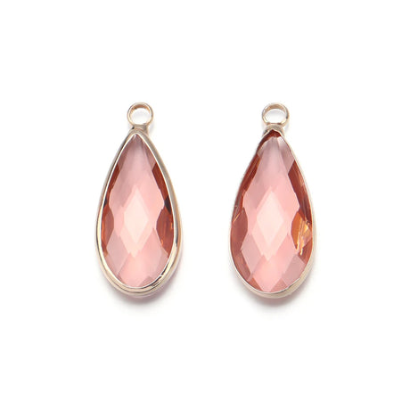 Two teardrop-shaped pink gemstones with gold settings on a white background