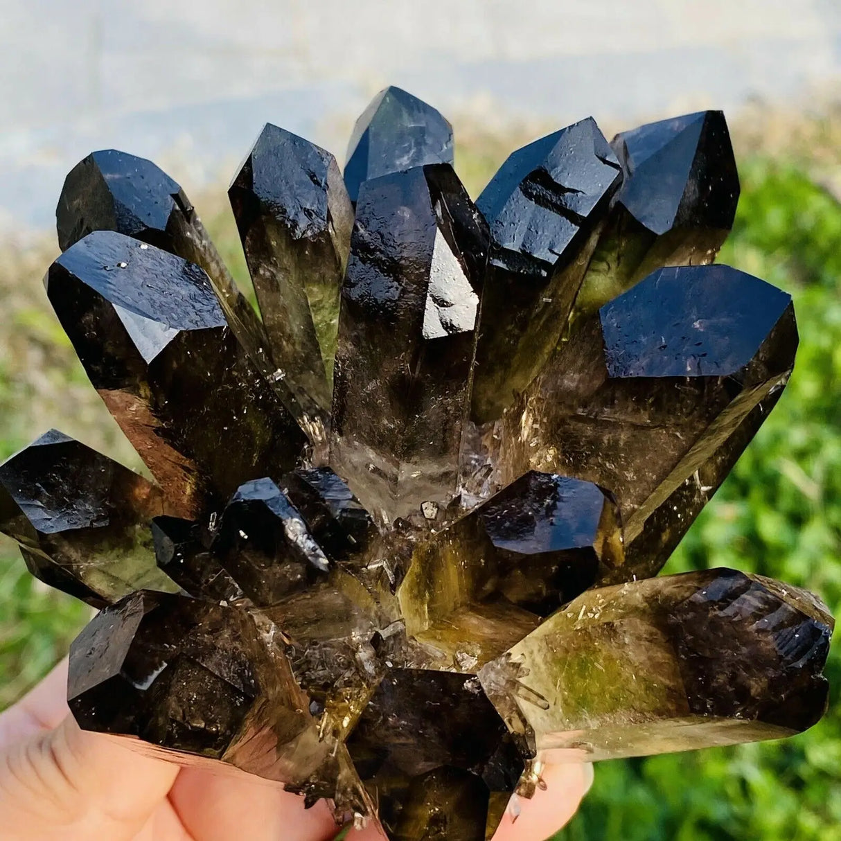 Smoky crystal cluster held by a hand with a natural background