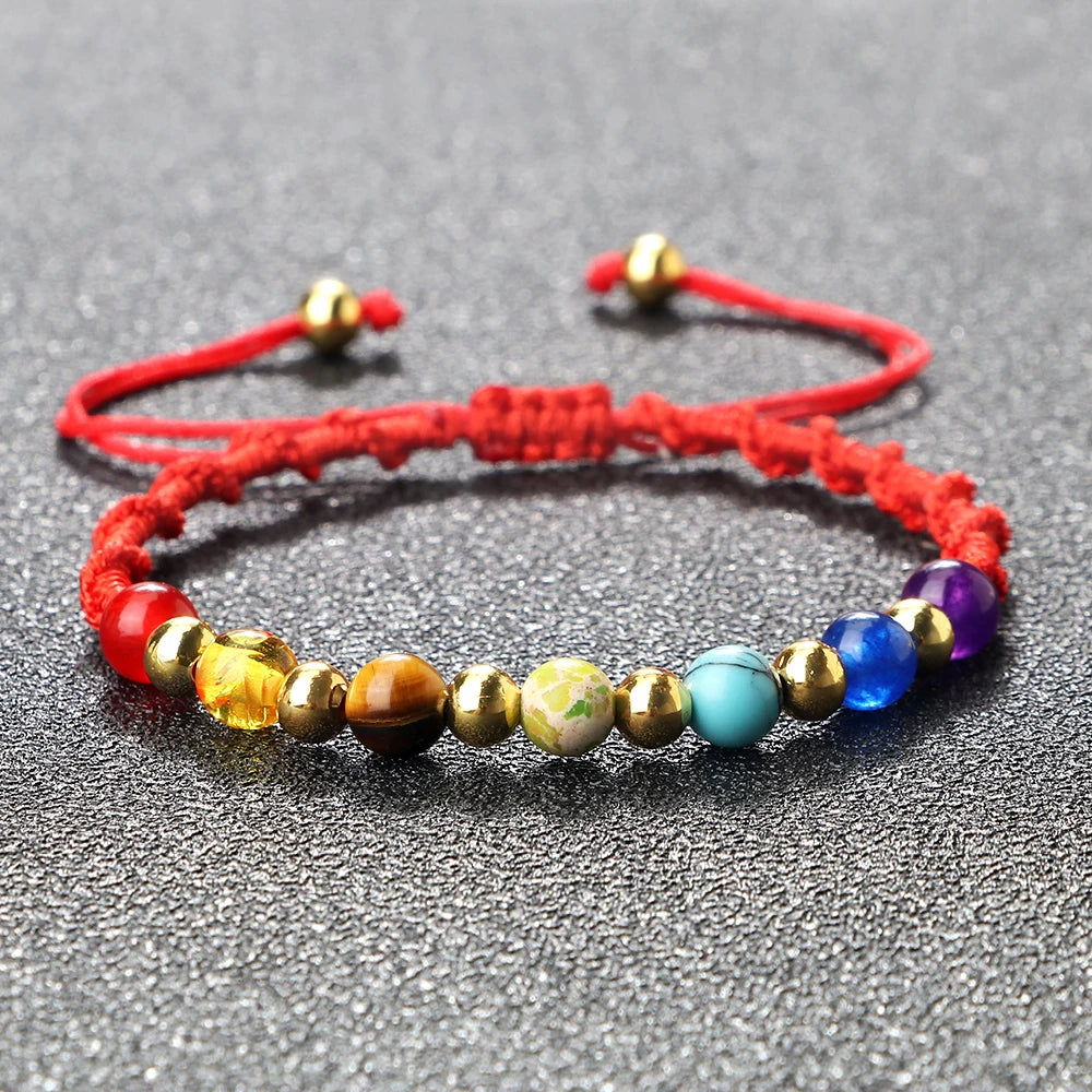 Multicolored beaded bracelet on a red string with gold clasps on a gray background