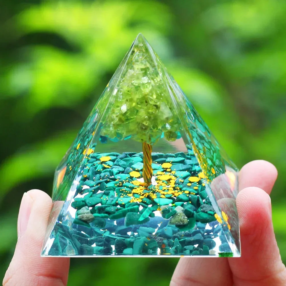 Pyramid-shaped crystal with green and yellow stones held by a hand against a blurred green background