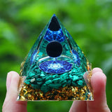 Triangular crystal with blue and green patterns held by a hand against a blurred green background