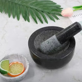 Black stone mortar and pestle on a light surface with lime and orange slices, and green leaves in the background.