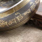 Close-up of a metal bowl with engraved text on a textured surface
