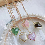Gold necklaces with heart-shaped gemstones on a textured surface