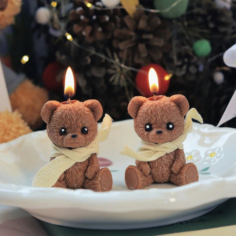 Two teddy bear-shaped candles with lit wicks on a white plate with a festive background.