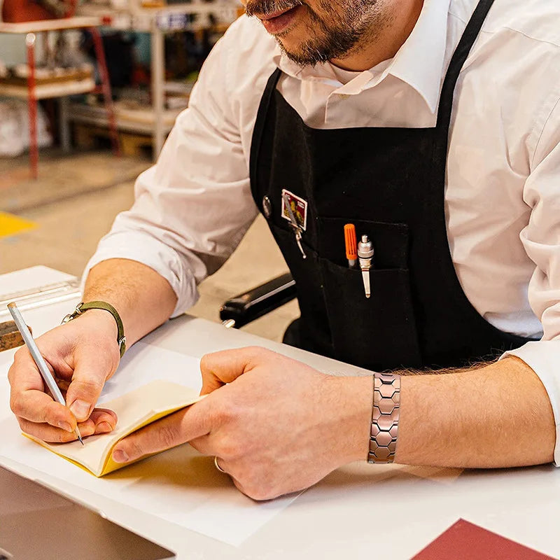 Person wearing a black apron and white shirt, writing in a notebook with a pen.