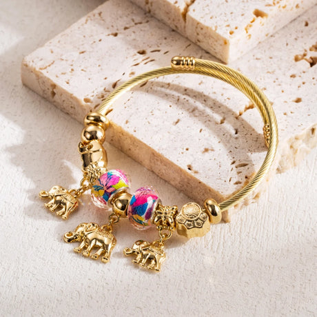 Gold bracelet with colorful charm on a textured stone surface