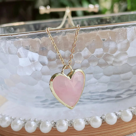 Heart-shaped pink pendant necklace on a gold chain against a decorative background