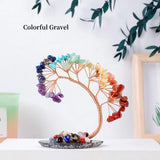 Colorful gravel arrangement in a decorative tree-like structure on a white surface with a plant in the background.